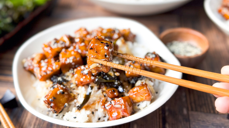 Crispy and sticky baked sesame tofu cube in chopsticks