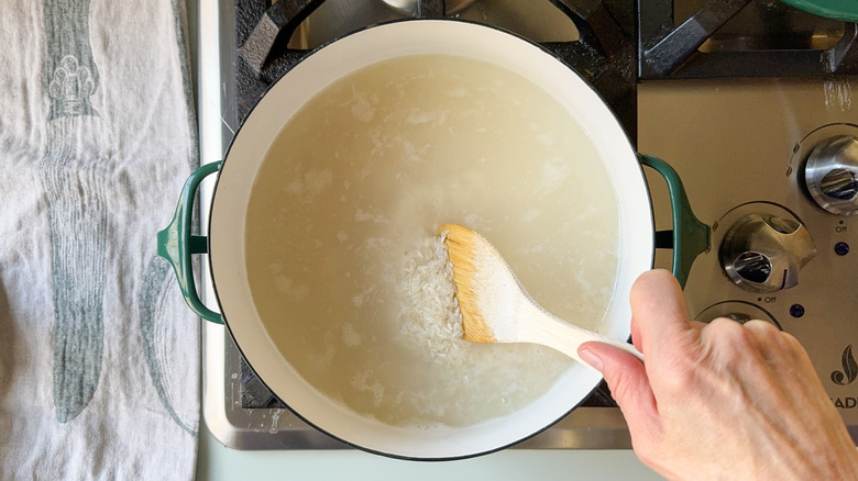 Stirring rice into water in pot with a wooden spoon on stovetop