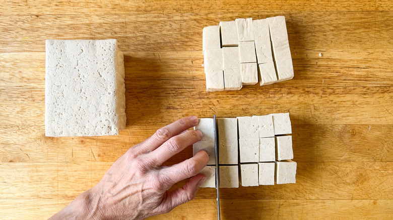 Cutting a block of firm tofu into cubes on cutting board