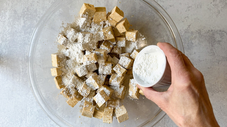 Sprinkling cornstarch over marinated tofu cubes in glass bowl