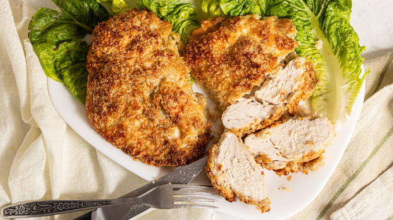 Two crispy coconut baked chicken breasts with one sliced on a bed of lettuce