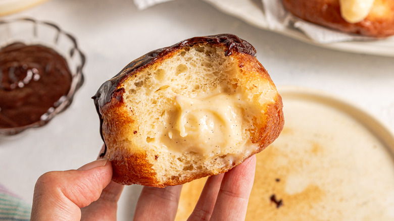 Holding custard-filled Boston cream donut with a bite taken off