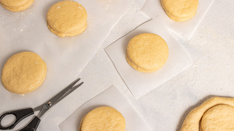 Round dough donuts each one on a piece of parchment paper