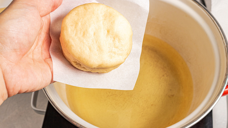 Holding donut on a parchment paper over a pot with oil