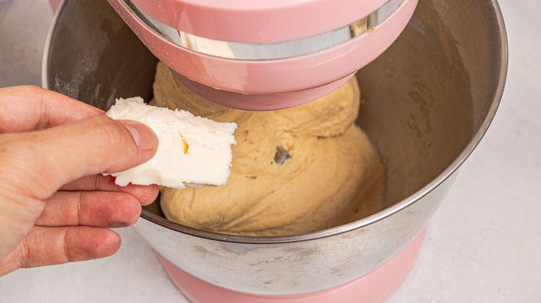 Adding butter to a stand mixer bowl with dough in it