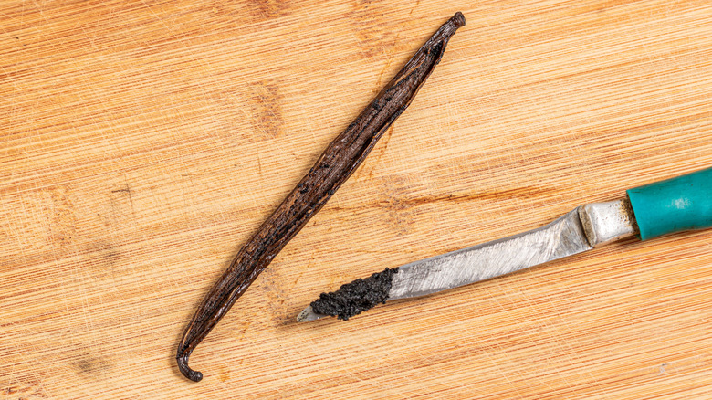 Vanilla bean sliced open with the seeds scraped out on a knife