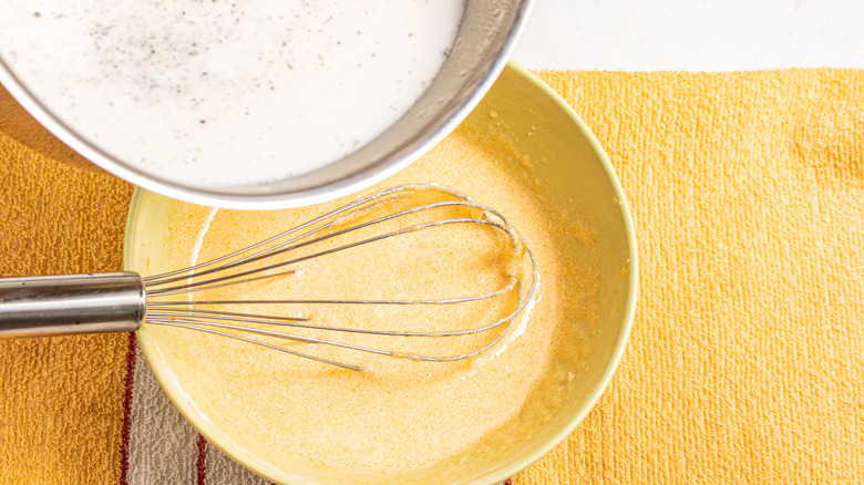 Pouring milk over a bowl with egg mixture and a whisk