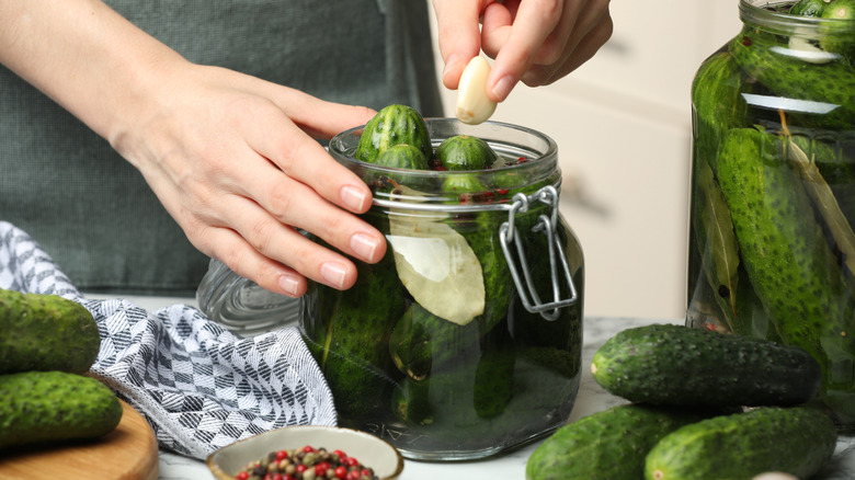 Person adding garlic glove to jar of pickles