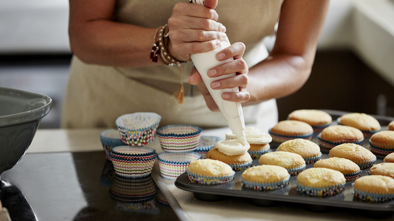 Person piping frosting onto cupcakes