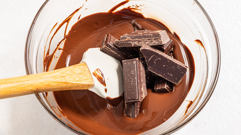 Bowl with melted chocolate and pieces of chocolate mixed in using a silicon spatula