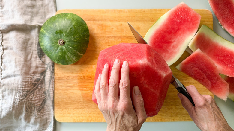 Removing rind from watermelon with chef's knife on cutting board