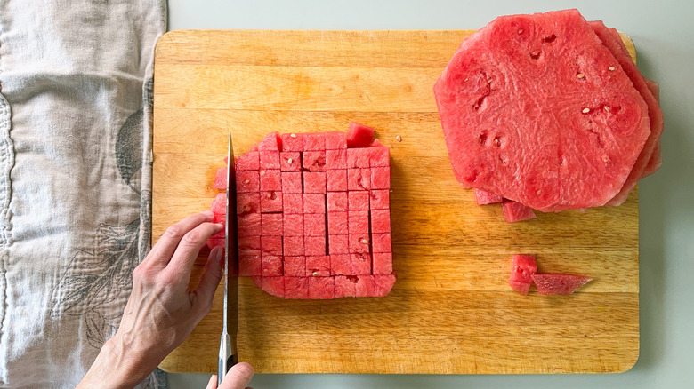 Cutting watermelon slices without rind into cubes on cutting board