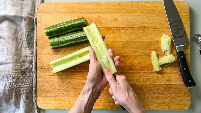Removing seed from English cucumber with vegetable knife on cutting board