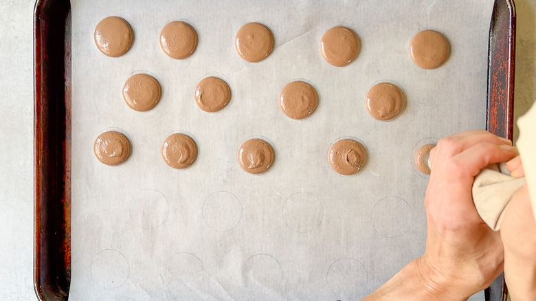 Piping chocolate macaron batter on parchment lined sheet pan