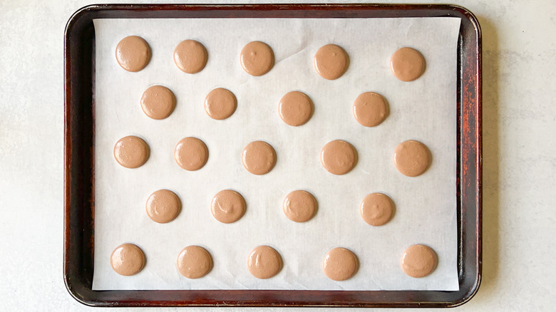 Piped chocolate macaron shells on baking sheet