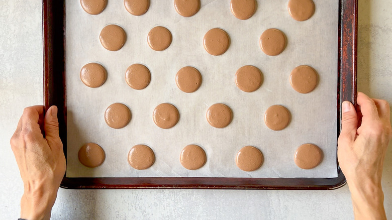 Tapping baking sheet with chocolate macaron shells to release air bubbles