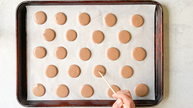 Using wooden pick to release air bubbles from chocolate macaron shells