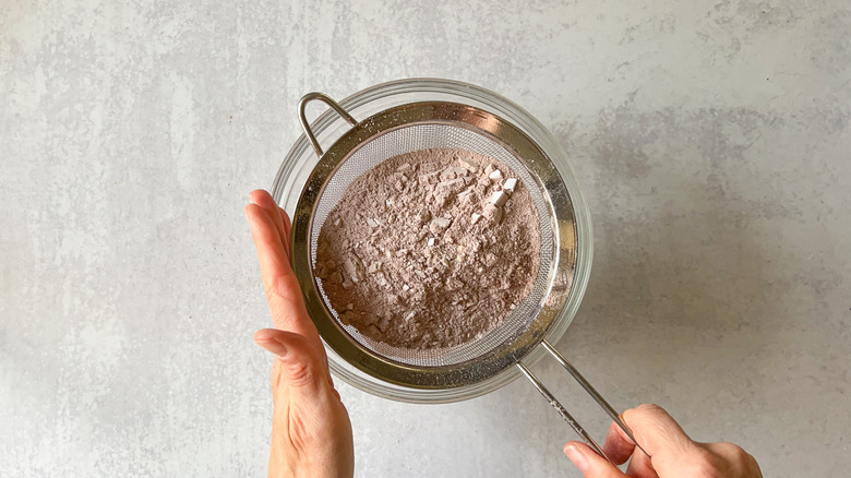Sifting chocolate macaron shell ingredients into bowl