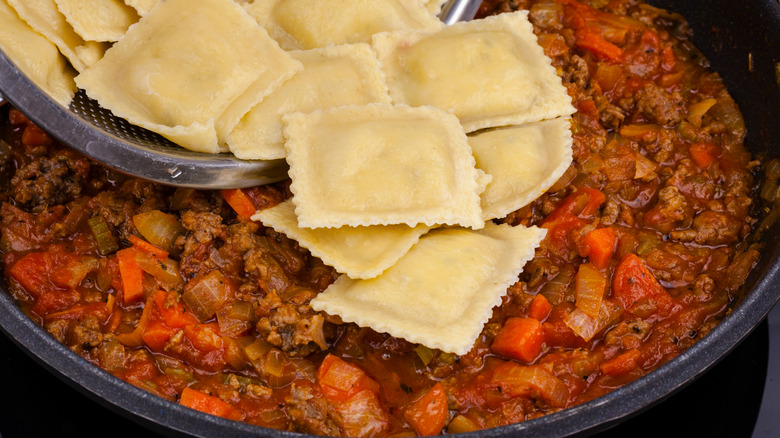 pouring ravioli from strainer into sauce