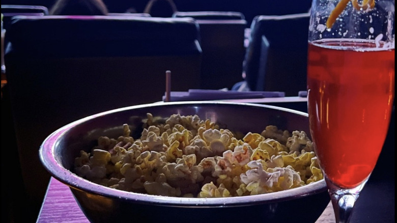 a bowl of popcorn and a red cocktail in a theater