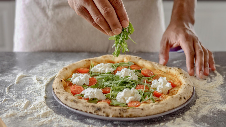 A person's hand adds arugula to a homemade pizza.
