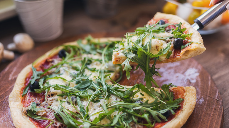 A slice of arugula piled pizza is removed with a spatula.