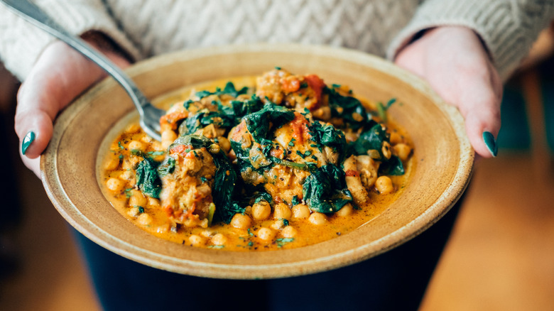 A woman presenting a bowl of chickpeas cooked with a variety of ingredients.