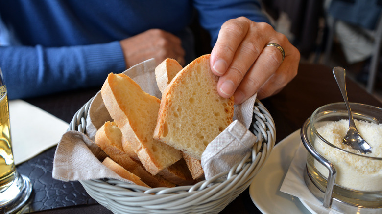 A hand grabbing bread from a basket on a table