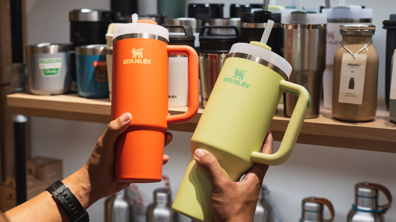 Two hands holding orange Stanley and yellow Stanley tumblers