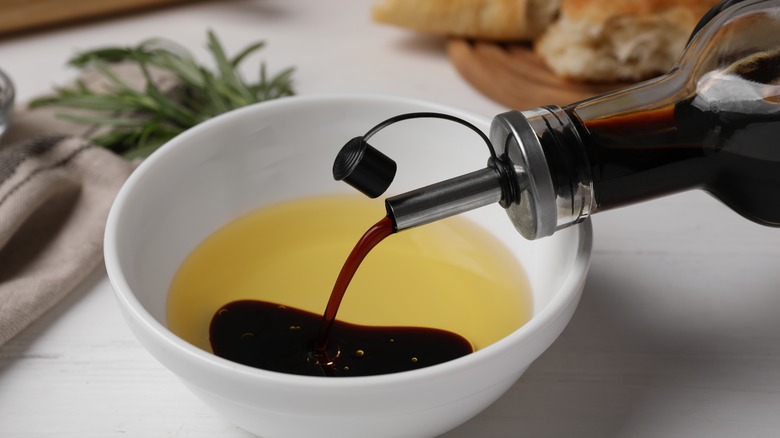 Balsamic vinegar being poured into oil inside a white dish