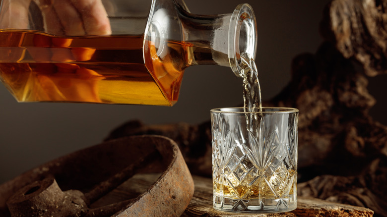 Whiskey is poured from a decanter in a dim, moody setting.