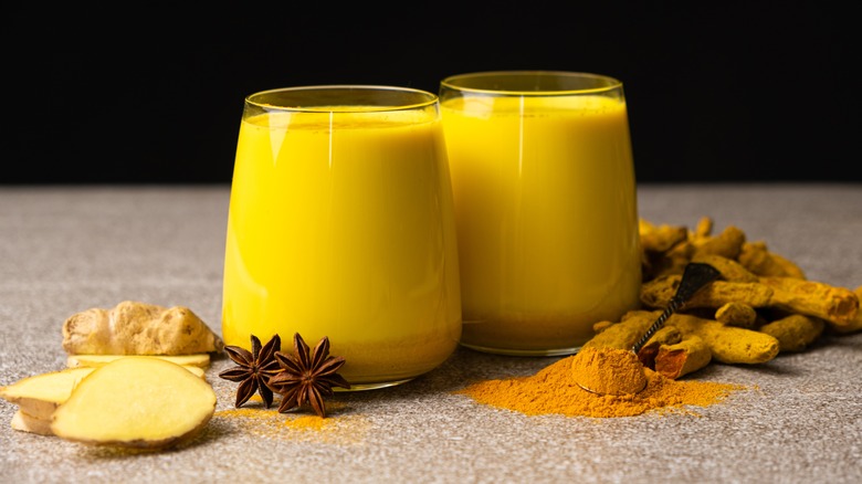 Two glasses of golden milk with dried herbs and seasonings