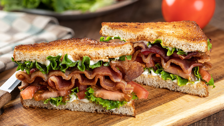 A built BLT with mayo on toast cut on the diagonal and placed on a cutting board