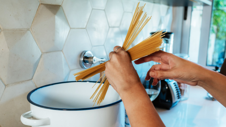 Person adding dried pasta to pot of water