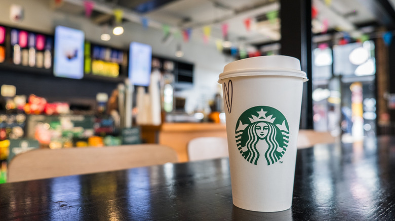 An interior of a Starbucks with a cup sitting on a table in the foreground.