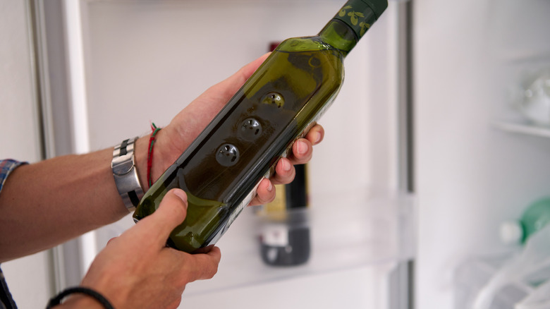 Holding bottle of olive oil in front of open refrigerator