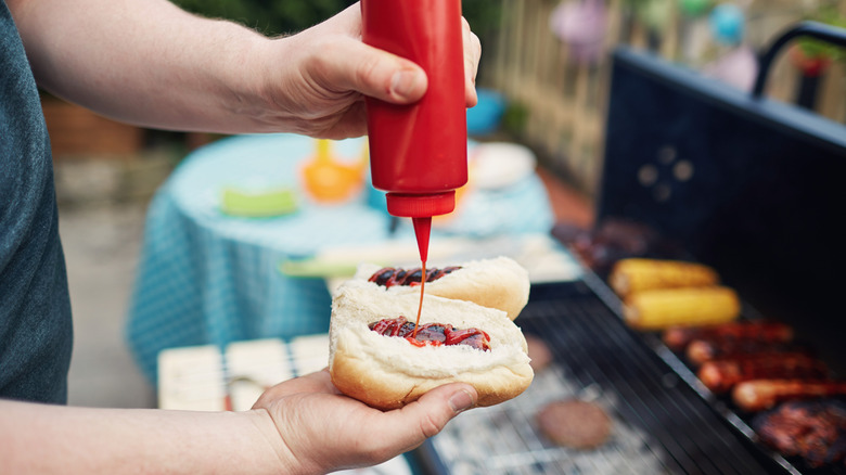 Man squirting ketchup onto a hot dog at a BBQ