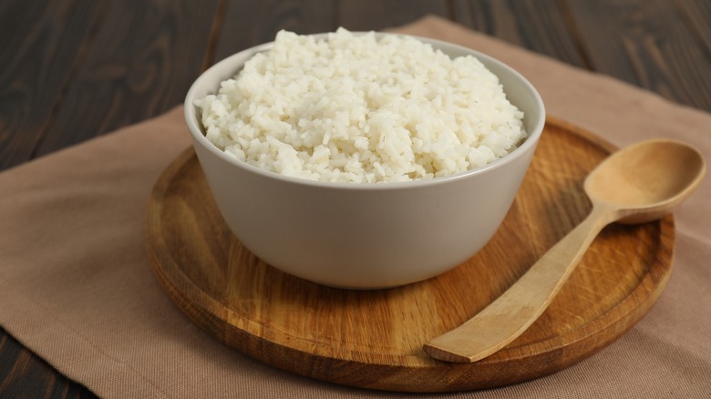 a bowl of rice next to a wooden spoon