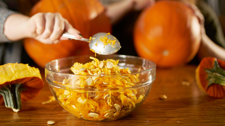 Person spooning pumpkin guts into a bowl