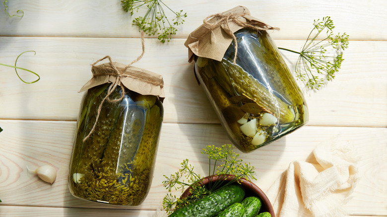 Artisinal pickled cucumbers in jars on wooden surface