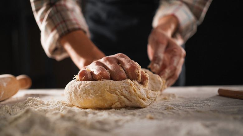 A persons hands make bread from dough on a floured surface.