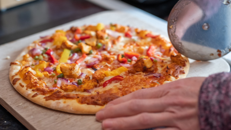 Close up of a thin crust sweet chilli chicken pizza on a wooden cutting board