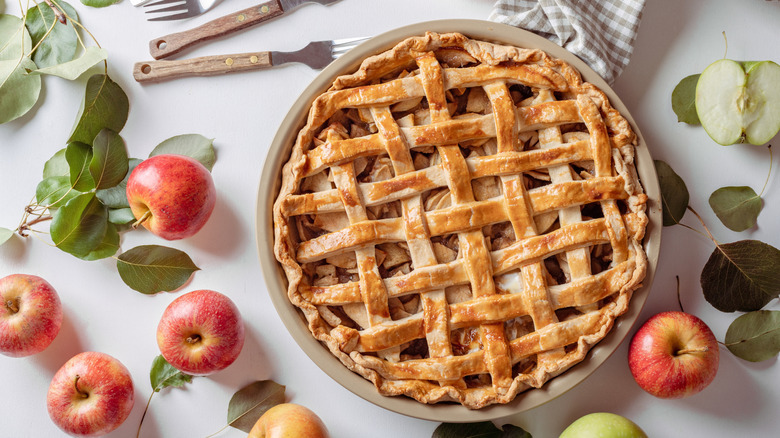 Apple pie plated next to whole apples