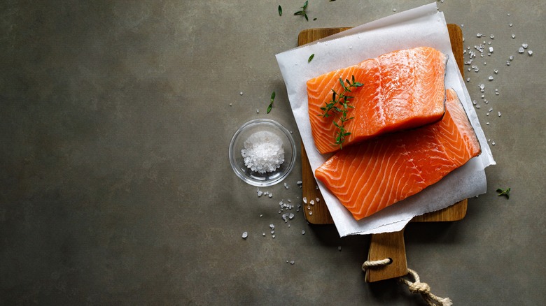 Raw salmon fillet on a wooden board with salt and herbs on the side