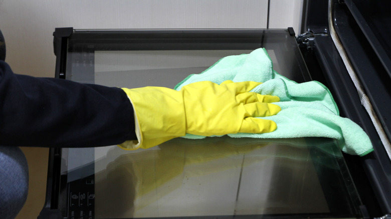 Gloved hand cleaning oven with rag