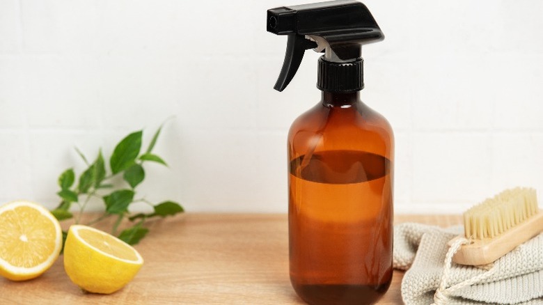 A bottle of natural cleaner sits on a wooden countertop next to lemons and a scrub brush.