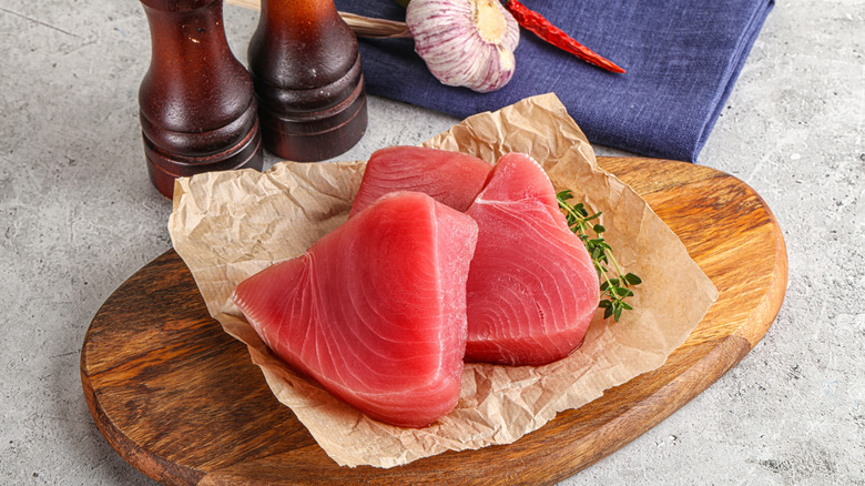 Tuna steaks resting on a cutting board beside salt and pepper grinders.