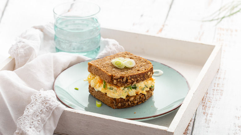An egg salad sandwich is piled high and served on a tray with a lacy napkin.