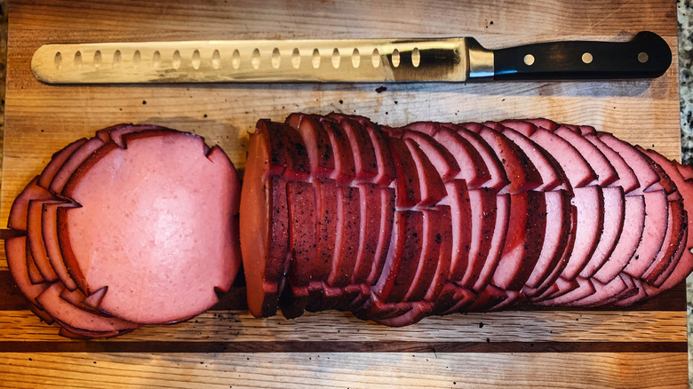 Slices of smoked bologna on a wooden cutting board next to a knife
