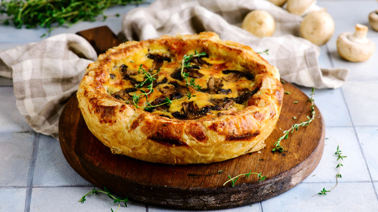 Rustic quiche on a wooden board with fresh herbs